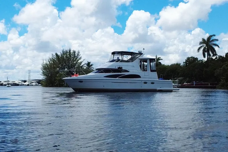 IV Play Too Yacht Photos Pics 2005 Carver 444 Cockpit Motor Yacht on calm water, surrounded by lush greenery.