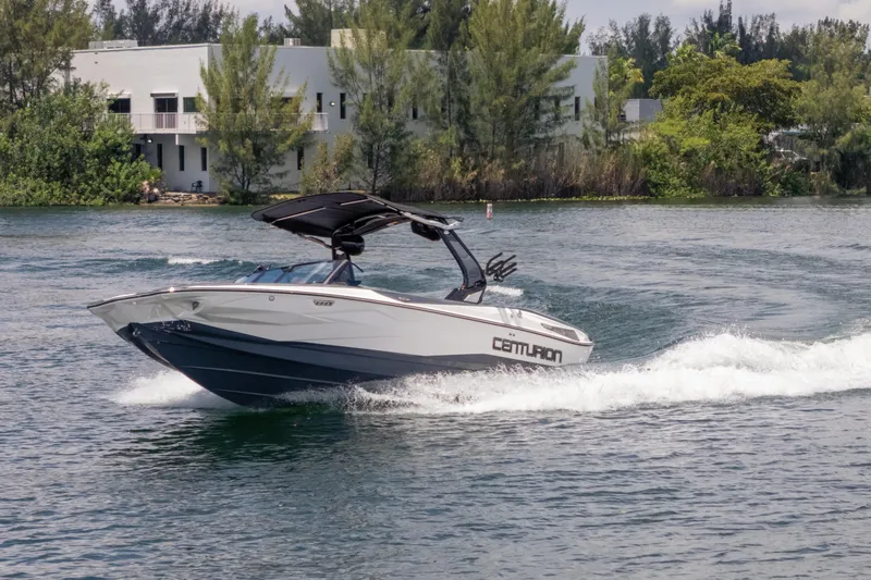  Yacht Photos Pics 2025 Centurion Nv233 boat cruising on a scenic lake with lush greenery.