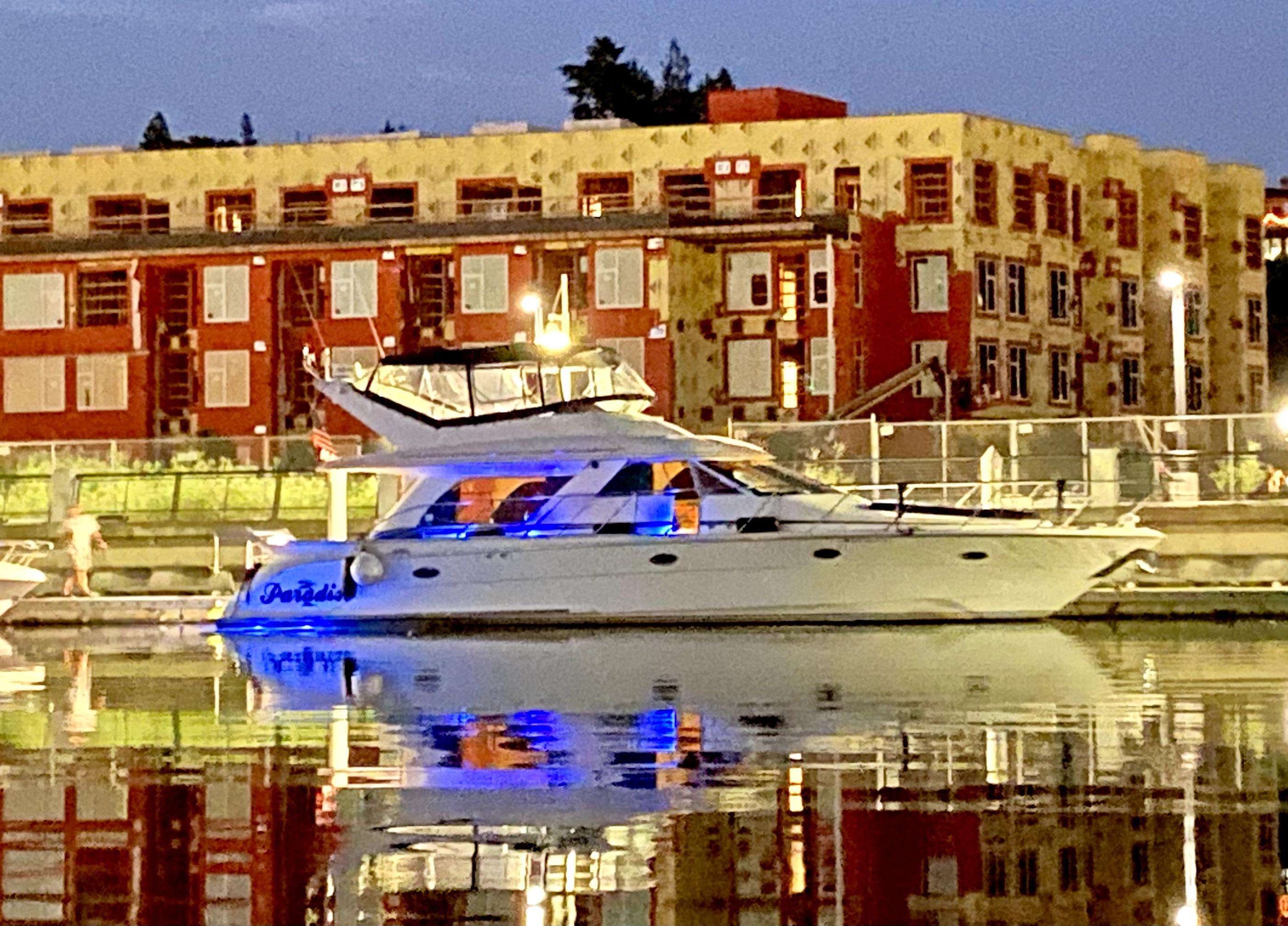 Luxury Prima 5230 yacht docked at night, reflecting on calm water, with illuminated buildings in background.