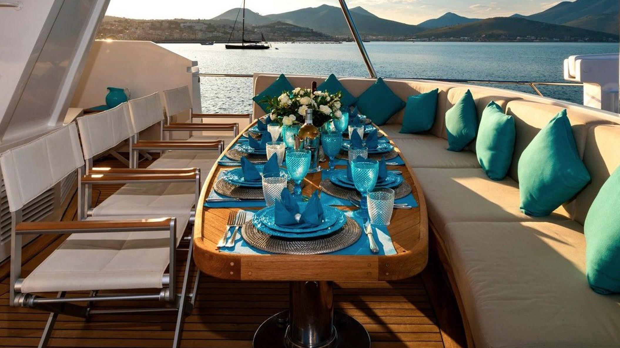 Luxurious yacht dining setup with blue accents, Codecasa 1987, overlooking serene waters and mountains.