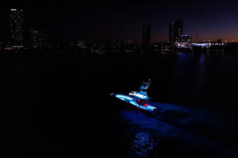 Toto II Yacht Photos Pics 2019 Mag Bay 33 CC boat illuminated at night, city skyline in background.