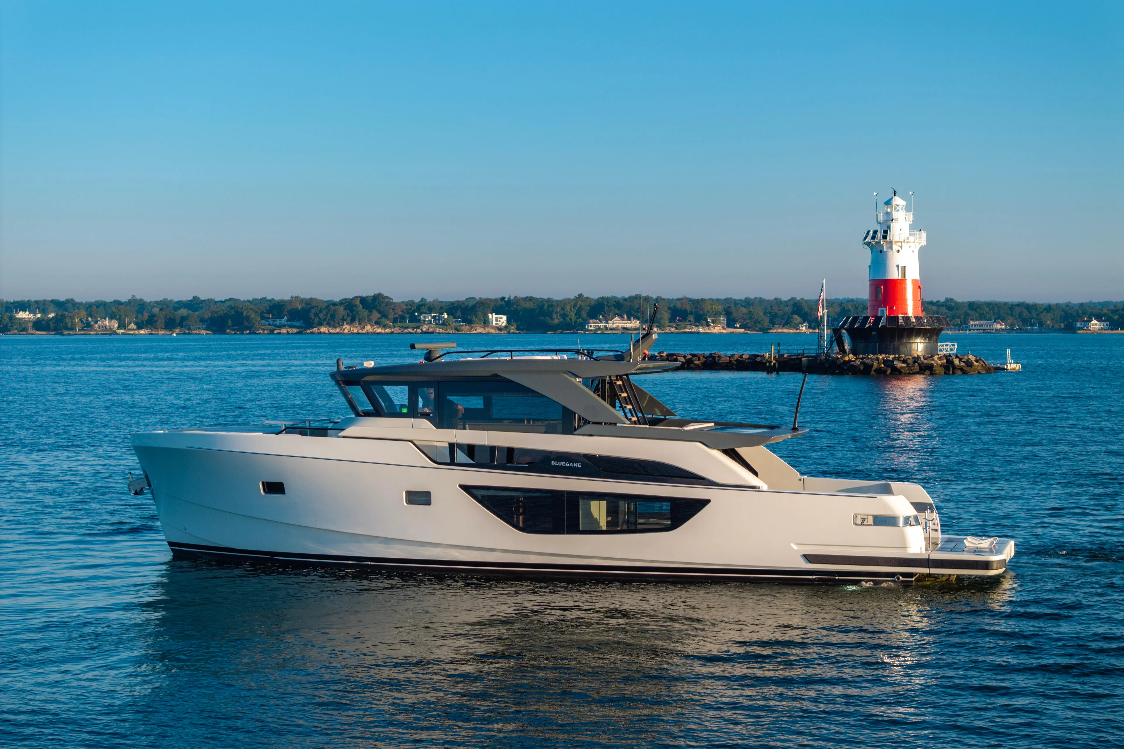 The Calm Down Yacht Photos Pics 2024 Bluegame BGX63 yacht cruising near a lighthouse on a sunny day.