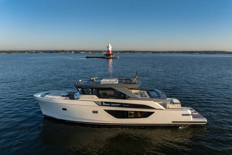 The Calm Down Yacht Photos Pics 2024 Bluegame BGX63 yacht cruising near a lighthouse on calm waters.