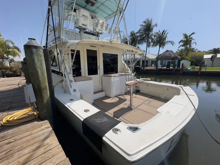 Laid Back Yacht Photos Pics 1983 Bertram 46 Convertible yacht docked by a wooden pier, surrounded by palm trees.