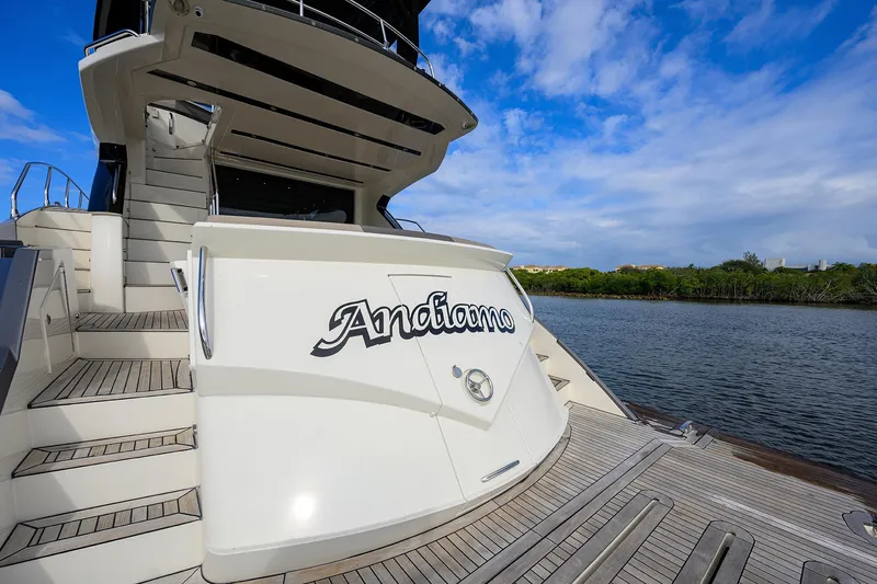Andiamo Yacht Photos Pics 2016 Marquis 660 Sport Yacht docked by a scenic waterway under a blue sky.