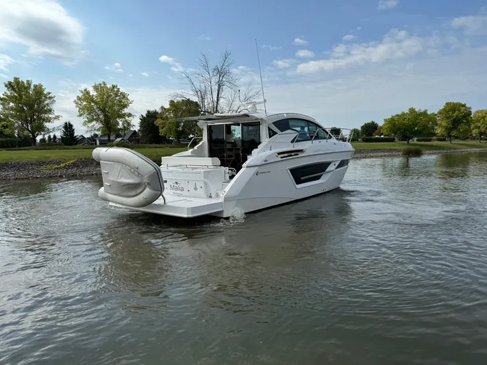  Yacht Photos Pics 2023 Cruisers Yachts 46 Cantius on calm water, surrounded by trees and blue sky.