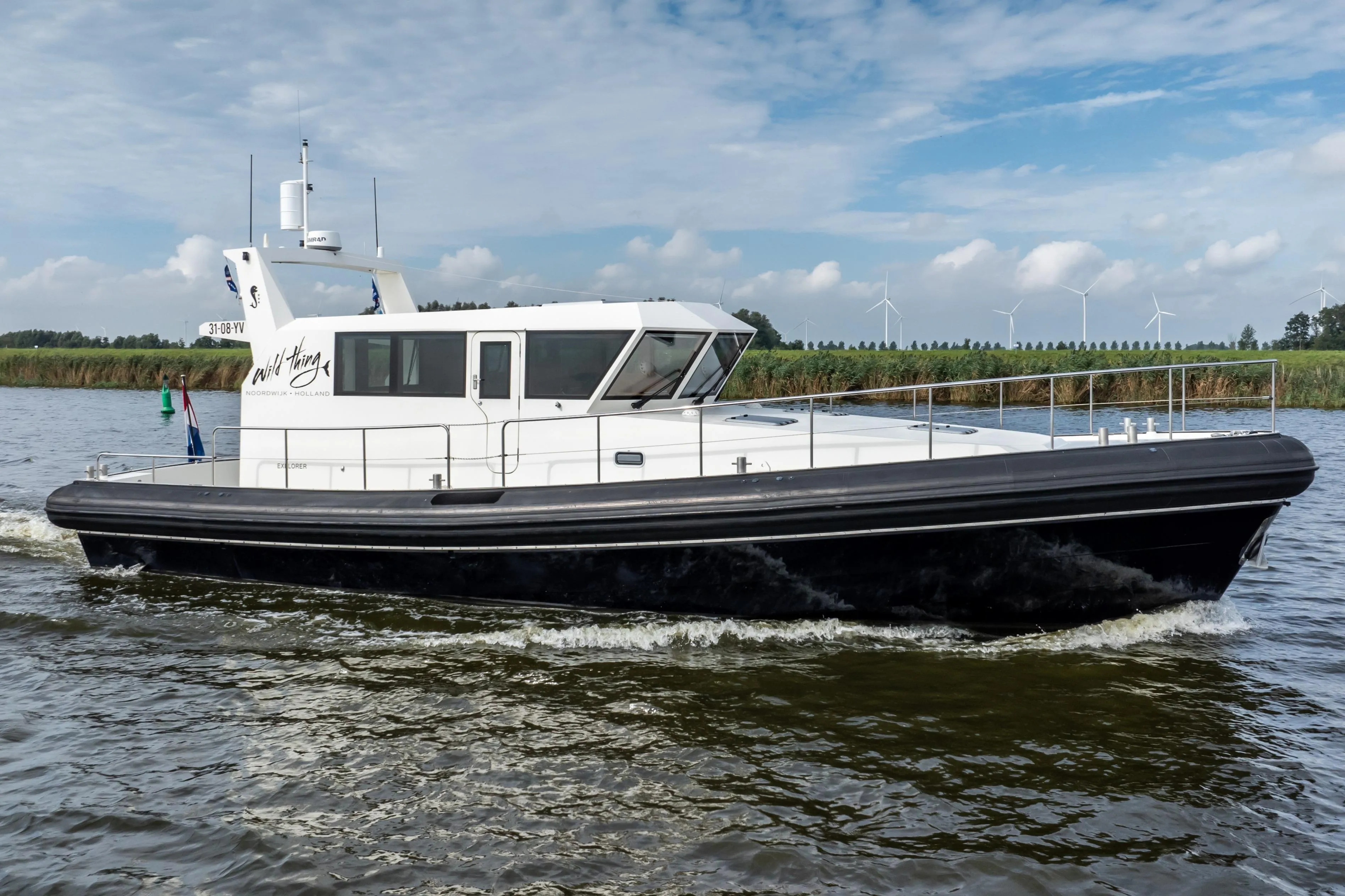 2016 Explorer NG 50 Alu Fast Going boat cruising on a river with wind turbines in background.