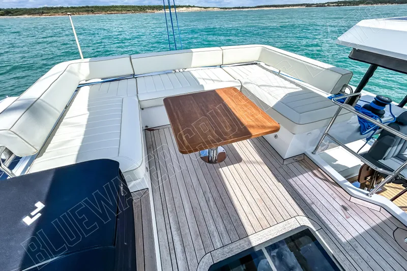Fun Pass Yacht Photos Pics Luxurious 2025 Privilege 580 yacht deck with white seating and wooden table, overlooking serene waters.