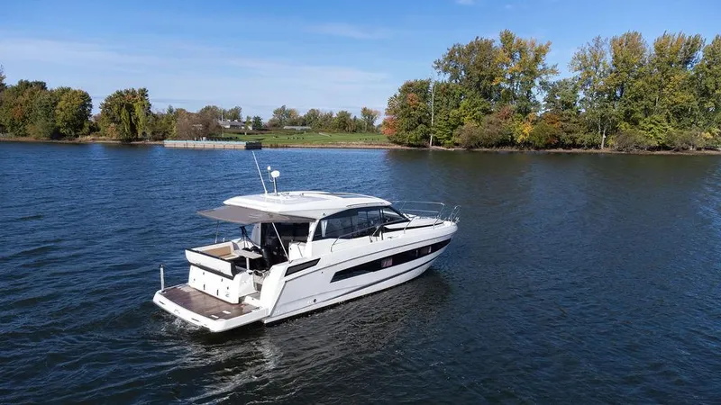  Yacht Photos Pics 2021 Jeanneau NC 37 yacht cruising on a serene lake with lush trees in the background.