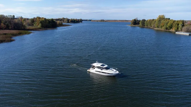  Yacht Photos Pics 2021 Jeanneau NC 37 cruising on a serene river surrounded by lush greenery.