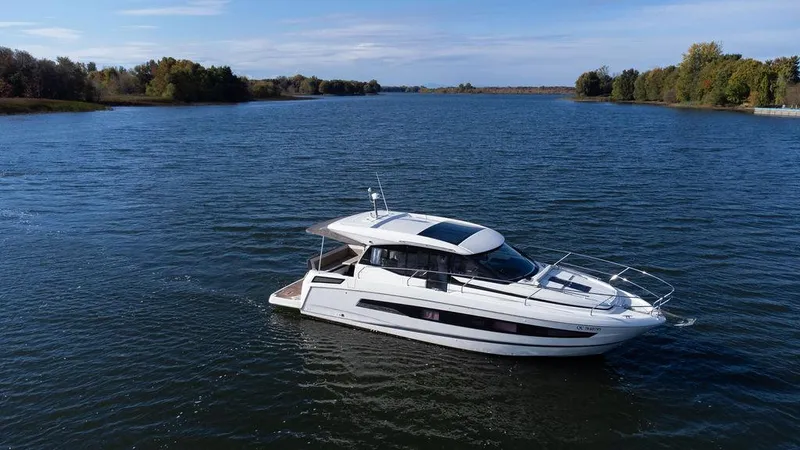  Yacht Photos Pics 2021 Jeanneau NC 37 yacht cruising on a serene lake with lush green surroundings.