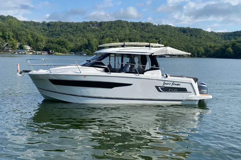  Yacht Photos Pics 2024 Jeanneau NC 895 boat on a serene lake with lush green hills.