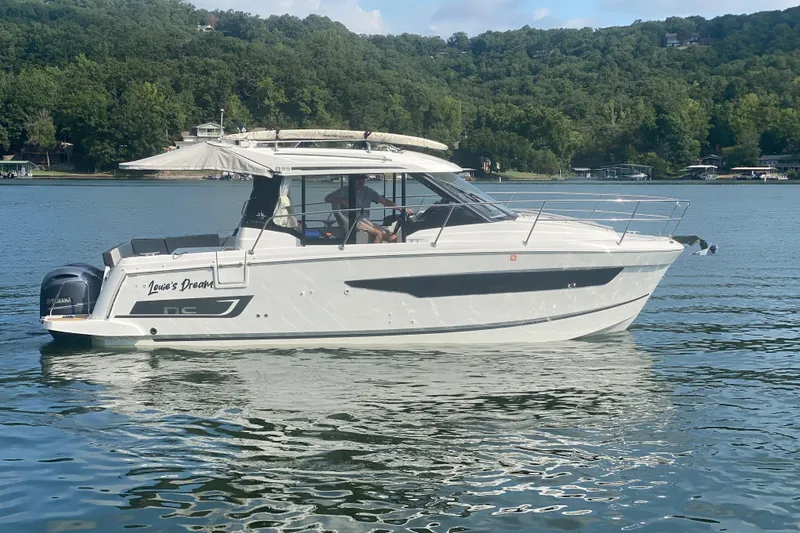  Yacht Photos Pics 2024 Jeanneau NC 895 boat on a serene lake with lush green hills.