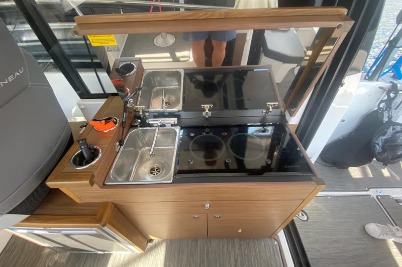  Yacht Photos Pics 2024 Jeanneau NC 895 boat kitchen with sink, stove, and wooden cabinetry.