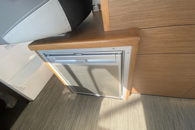  Yacht Photos Pics 2024 Jeanneau NC 895 interior with compact built-in refrigerator and wooden cabinetry.