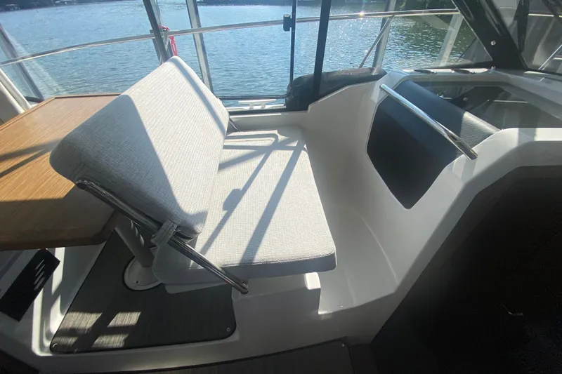  Yacht Photos Pics 2024 Jeanneau NC 895 interior with cushioned seating and wooden table by the window.