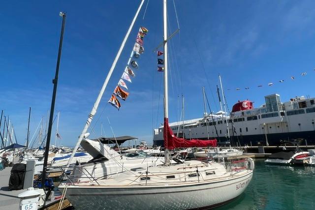 1986 Pearson 303 sailboat docked at marina, adorned with colorful flags under clear blue sky.