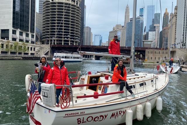 Group on 1986 Pearson 303 sailboat "Bloody Mary" in urban waterway, city skyline background.