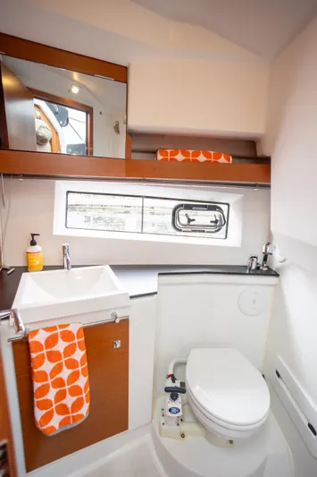 Myrt Yacht Photos Pics Bathroom interior of 2016 Jeanneau NC9 boat with modern fixtures and orange accents.