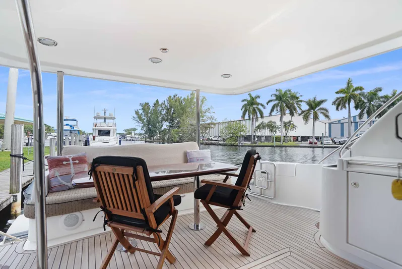 Carrie Ann Yacht Photos Pics Outdoor seating area on 2006 Neptunus 62 Flybridge yacht, featuring wooden chairs and table.