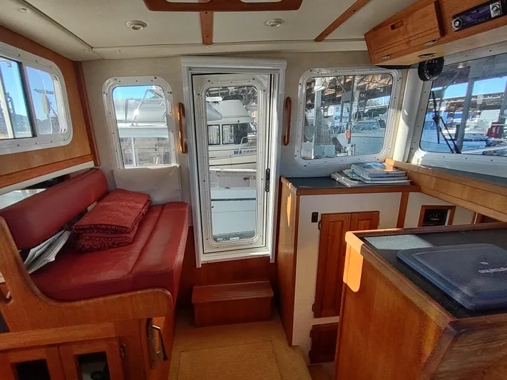 Santosha Yacht Photos Pics Interior of a 2006 Nordic Tug 32 boat with red seating and wooden cabinetry.