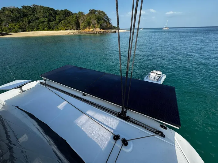 Primrose Yacht Photos Pics 2023 Lagoon 46 catamaran with solar panel, anchored near a tropical beach.