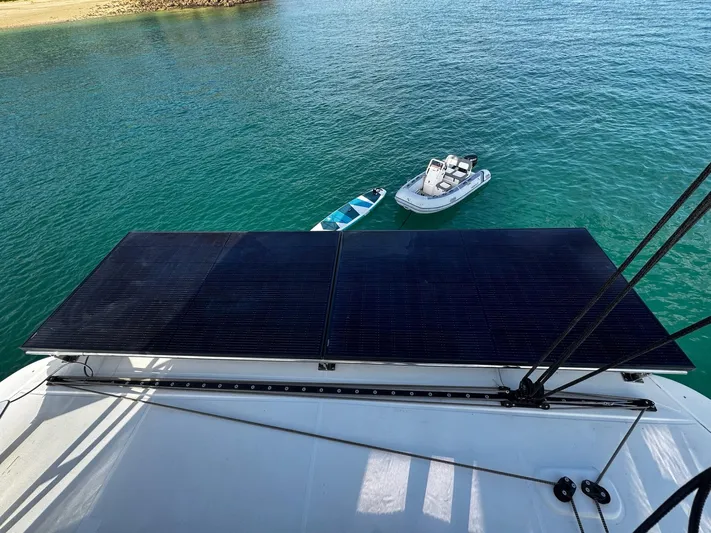 Primrose Yacht Photos Pics 2023 Lagoon 46 catamaran with solar panels, paddleboard, and dinghy on turquoise water.