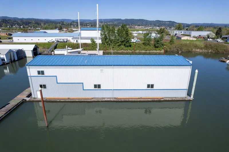  Yacht Photos Pics Aerial view of 1985 Custom Larson Boathouse on calm water, blue roof, industrial background.