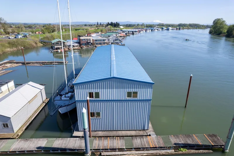  Yacht Photos Pics Blue boathouse on calm river, surrounded by docks and trees, under clear sky.