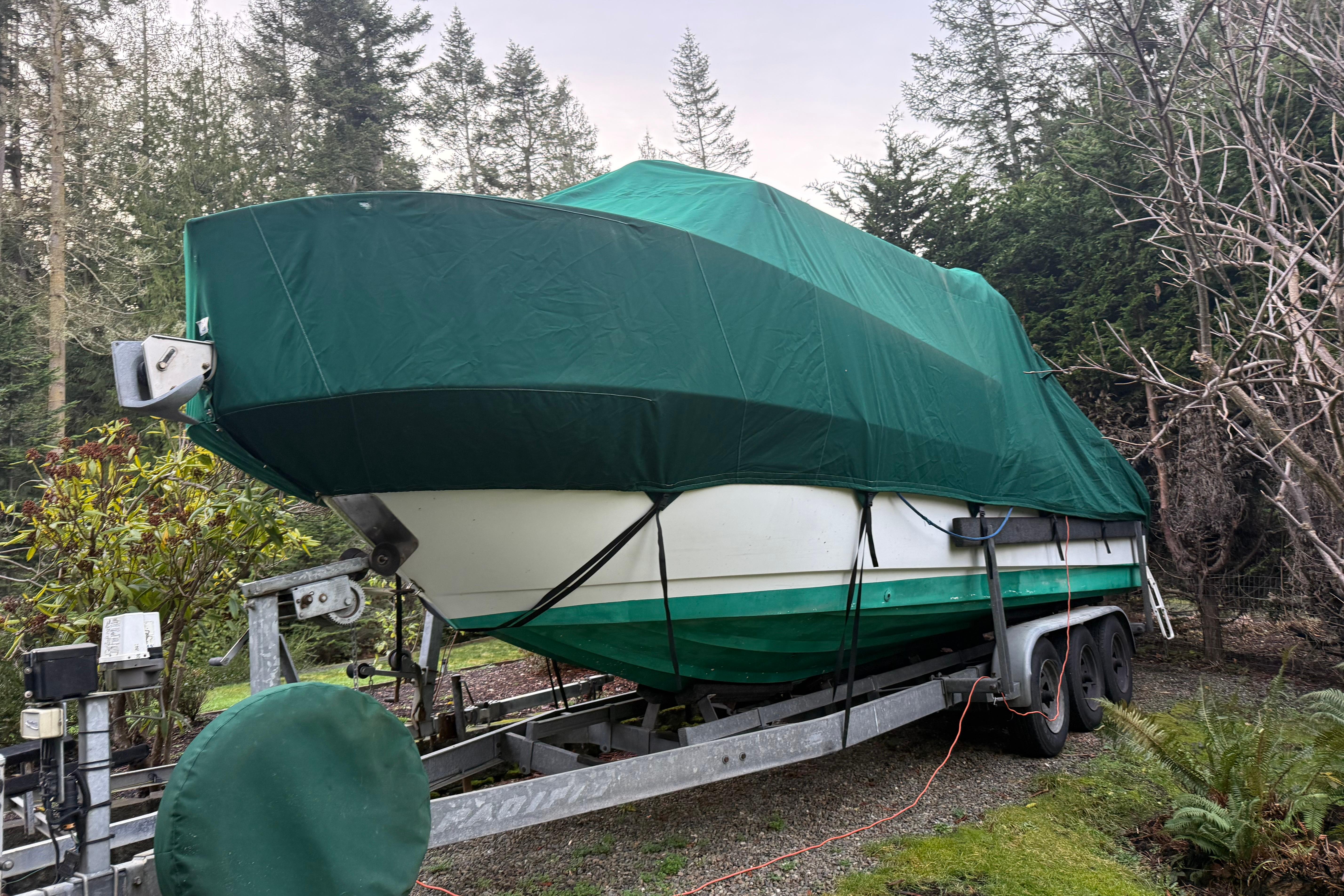 1998 Davis Rock Harbor 25 boat covered with green tarp on trailer in wooded area.
