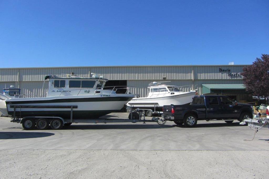 1998 Davis Rock Harbor 25 boat on trailer, parked outside a warehouse under clear blue sky.