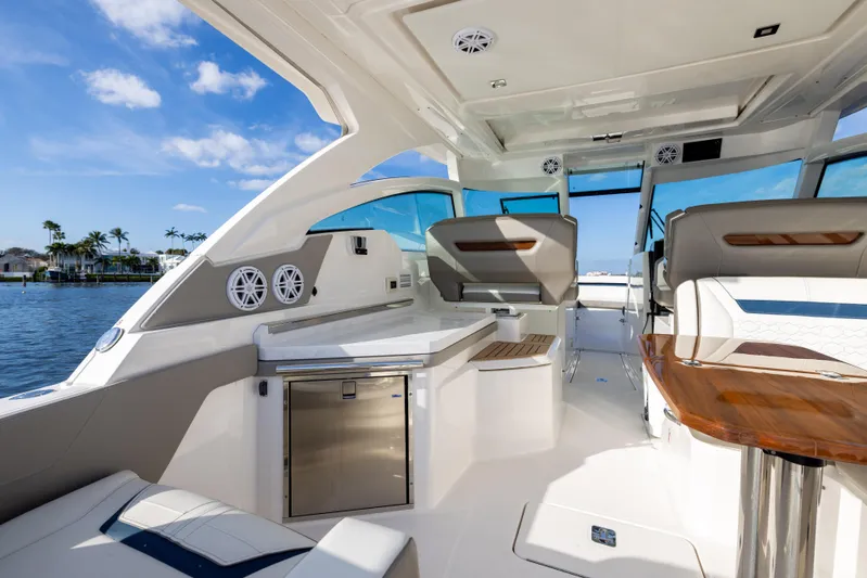 34 Tiara 2022 Yacht Photos Pics 2022 Tiara 34 LX luxury boat interior with seating and table, overlooking water and palm trees.