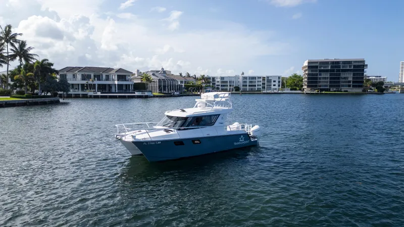 Transcendent Yacht Photos Pics 2023 ArrowCat Flybridge Dual Helm boat on a calm waterway with modern buildings in the background.
