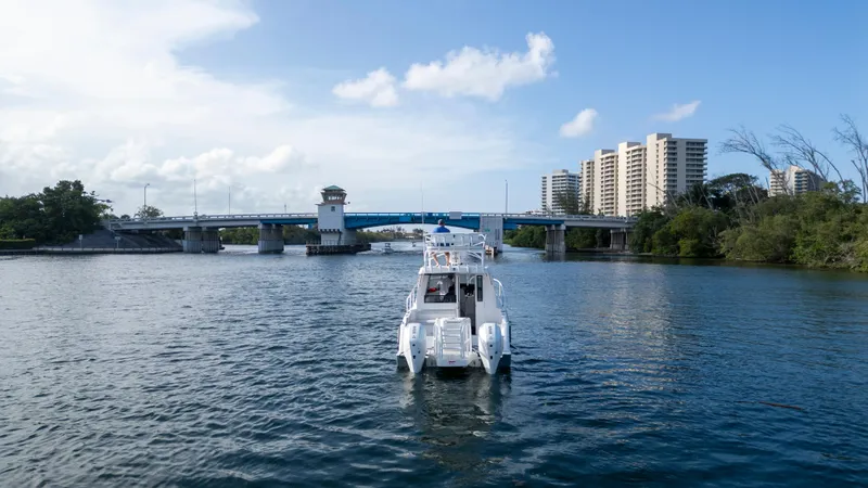 Transcendent Yacht Photos Pics 2023 ArrowCat Flybridge Dual Helm boat cruising near a bridge with cityscape background.