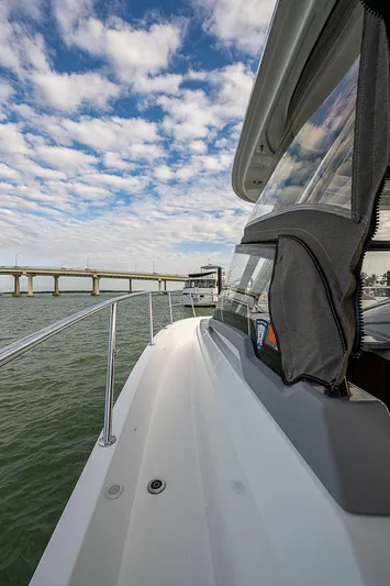 Brama Sole Yacht Photos Pics 2022 Jeanneau Leader 12.5 yacht cruising near a bridge under a partly cloudy sky.