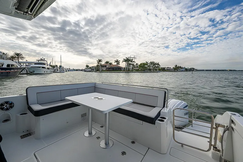 Brama Sole Yacht Photos Pics 2022 Jeanneau Leader 12.5 boat deck with seating and table, overlooking a scenic waterfront.