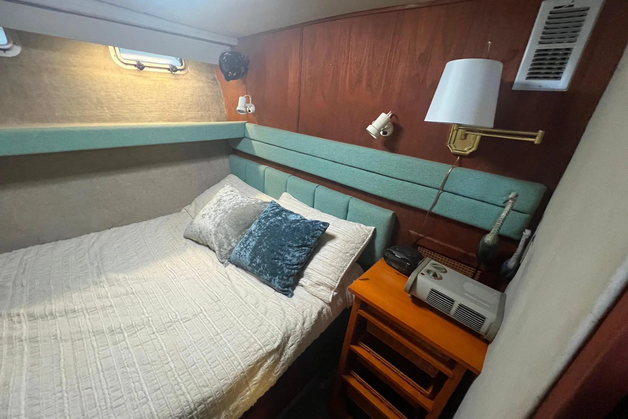 Cozy bedroom in 1986 Bayliner 4550 Motoryacht with bed, pillows, and wooden nightstand.