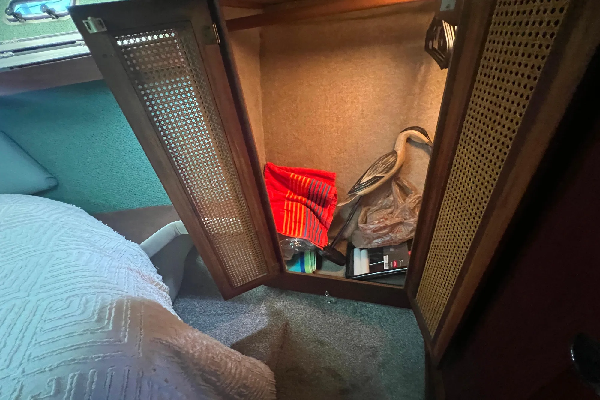 Open cabinet in 1986 Bayliner 4550 Motoryacht with decorative items and textiles inside.