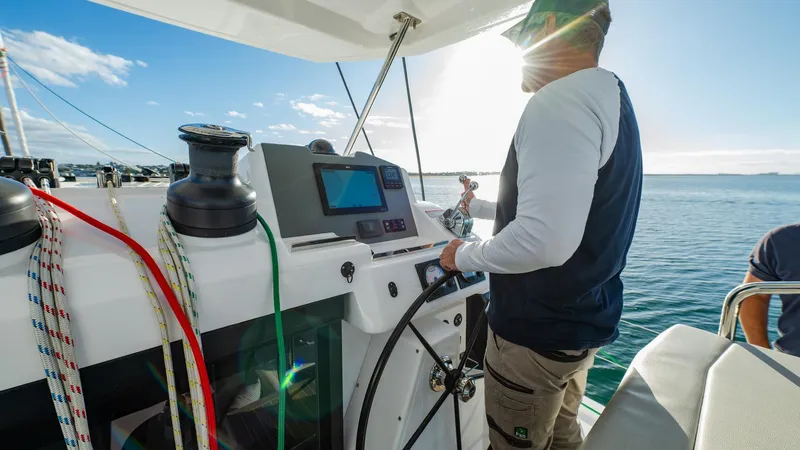  Yacht Photos Pics Person steering 2024 Leopard 50 yacht, sunny day, ocean view, colorful ropes, navigation equipment.