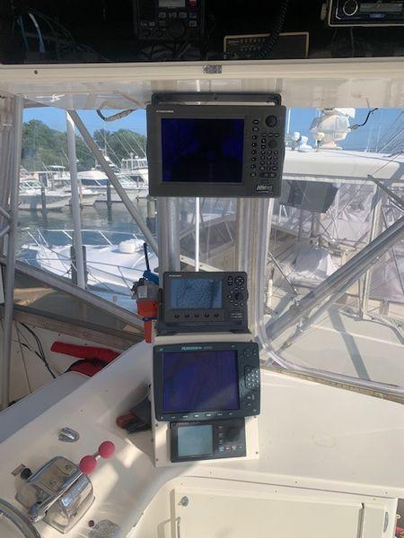 Boat cockpit with navigation equipment, featuring multiple screens and controls, docked at a marina.