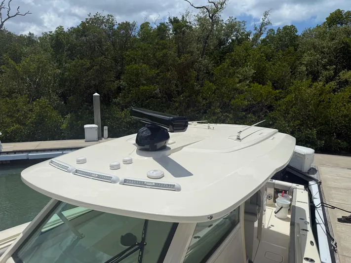  Yacht Photos Pics 2022 Scout 425 LXF boat roof with radar, docked near lush greenery.