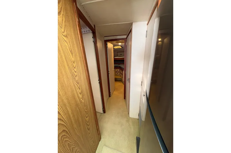 Sea Legs Yacht Photos Pics Narrow hallway inside 1987 Bertram 46.6 yacht, featuring wood paneling and carpeted floor.