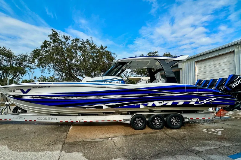  Yacht Photos Pics 2024 MTI V42 boat with blue and white design on a trailer, parked outdoors.