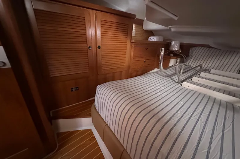 True North Yacht Photos Pics Cozy cabin interior of 2003 Catalina 470 sailboat with striped bedding and wooden cabinetry.