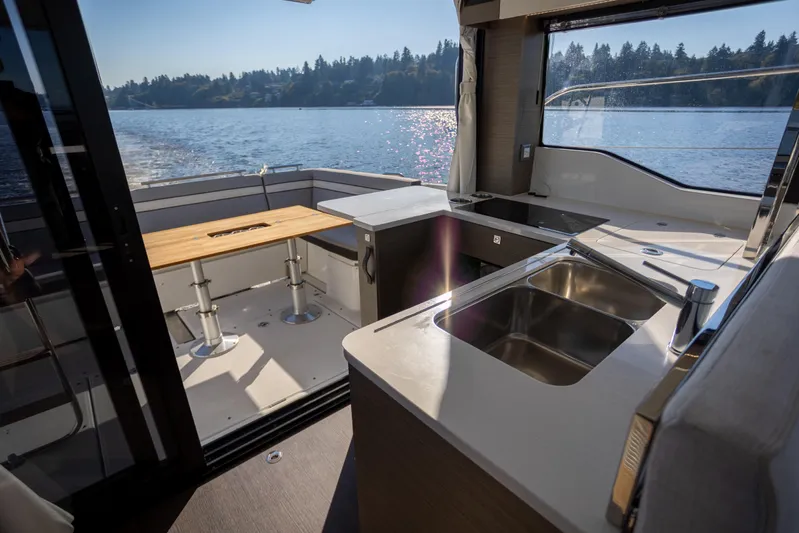 Samadhi Yacht Photos Pics 2024 Jeanneau NC 1295 Fly yacht interior with kitchen and dining area overlooking water.