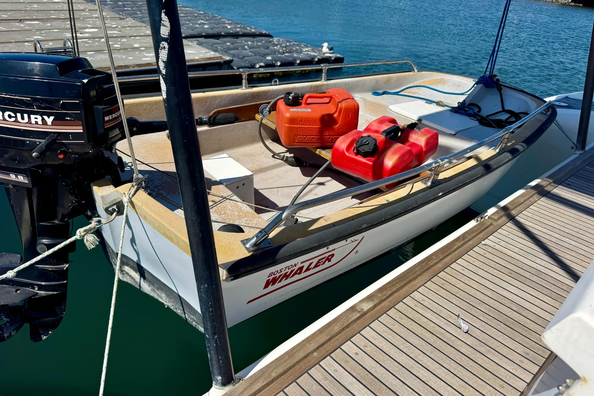 Small boat with Mercury outboard motor docked, featuring fuel containers on deck.