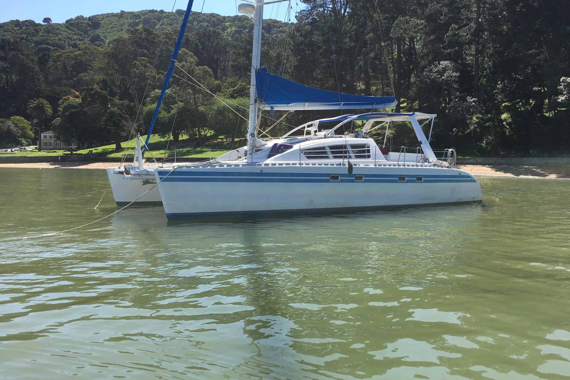 1992 Wauquiez Kronos catamaran anchored near a lush, forested shoreline.