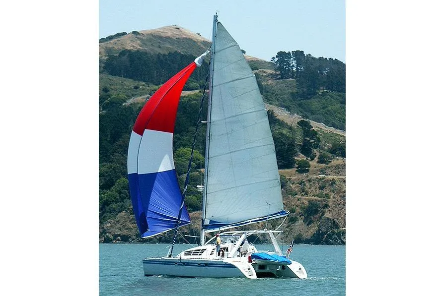 Sailing catamaran Wauquiez Kronos 1992 with colorful spinnaker on scenic water.