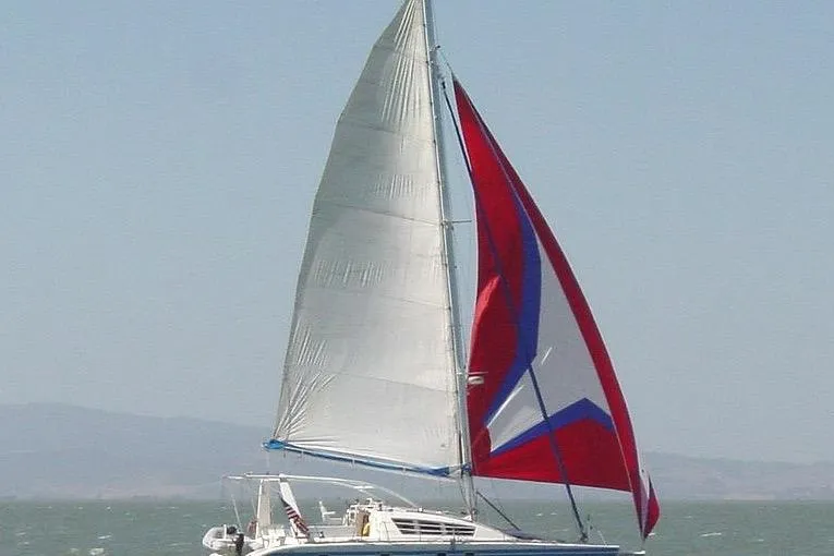 Sailing yacht Wauquiez Kronos 1992 with vibrant red and blue sails on open water.