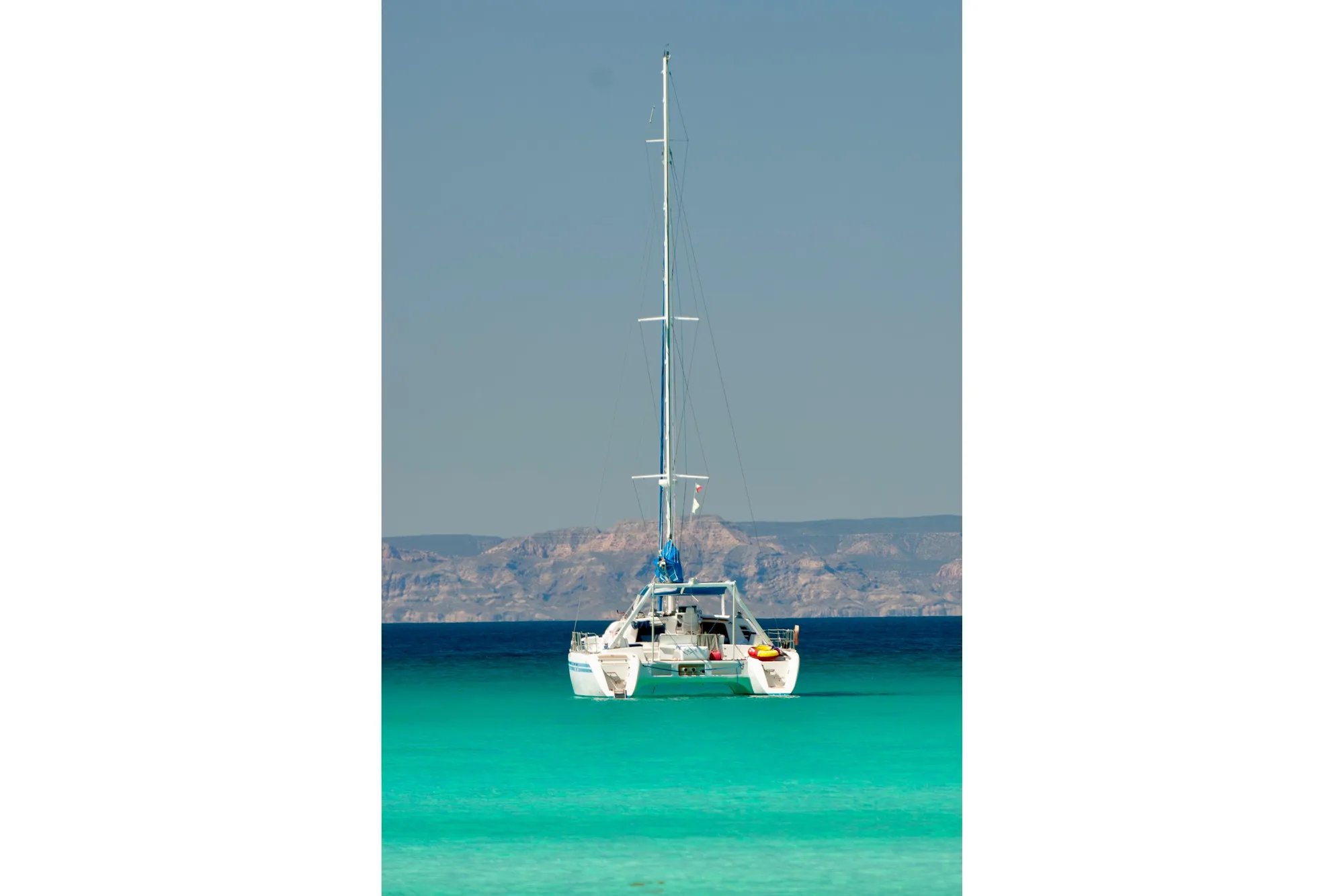 Sailing catamaran Wauquiez Kronos 1992 on turquoise sea with mountainous backdrop.